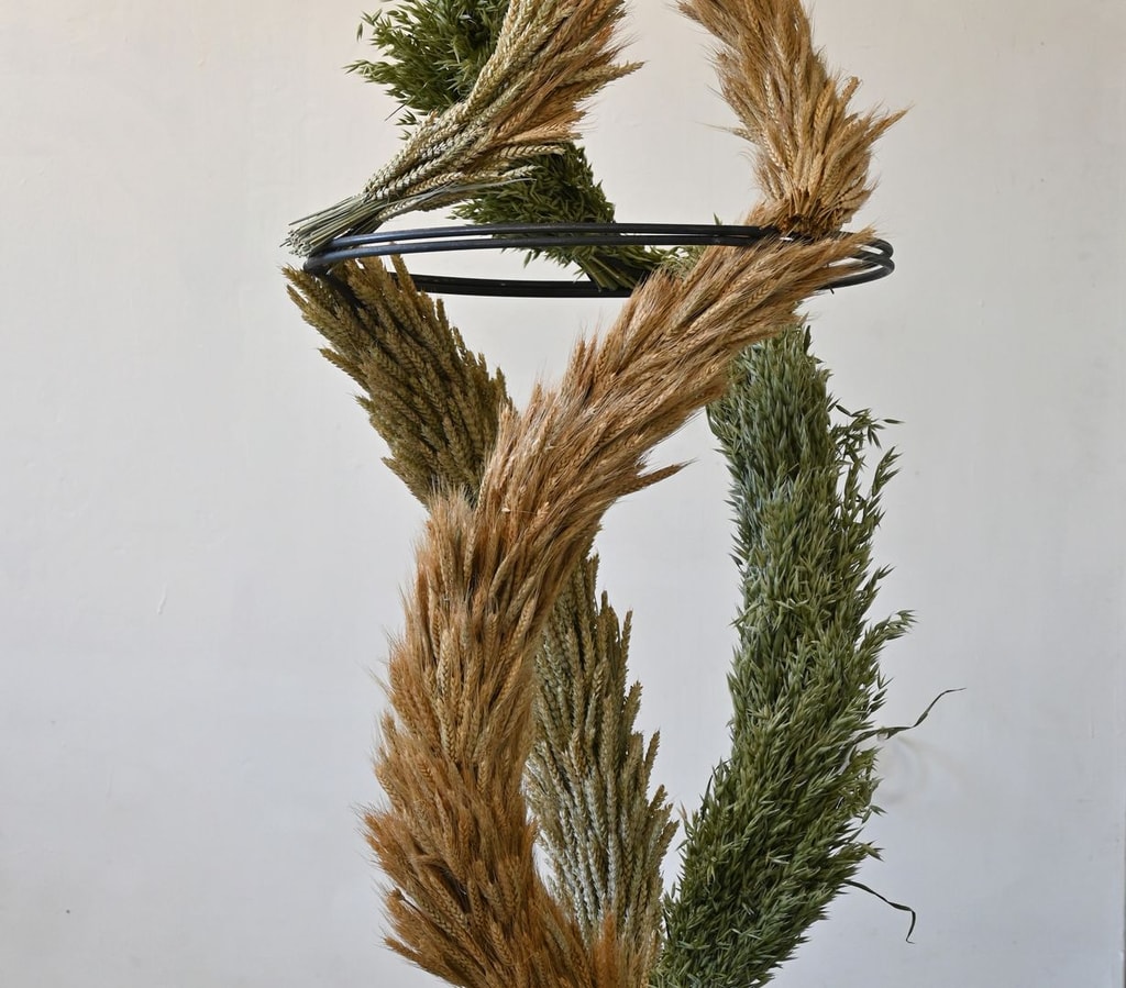 Sculpture by Lucie Kordacova made from three garlands of wheat (brown, yellow, and green) swirling around a metal armature and joining at the top.