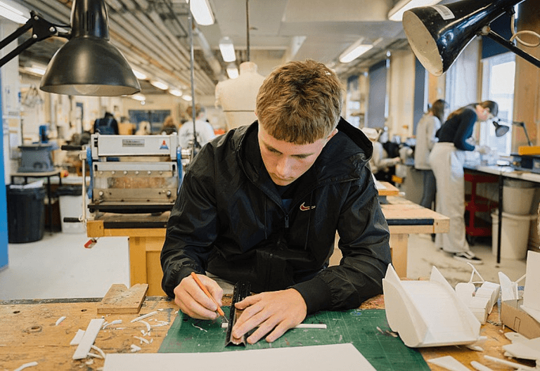 A blonde male student working on a project on a cutting board.