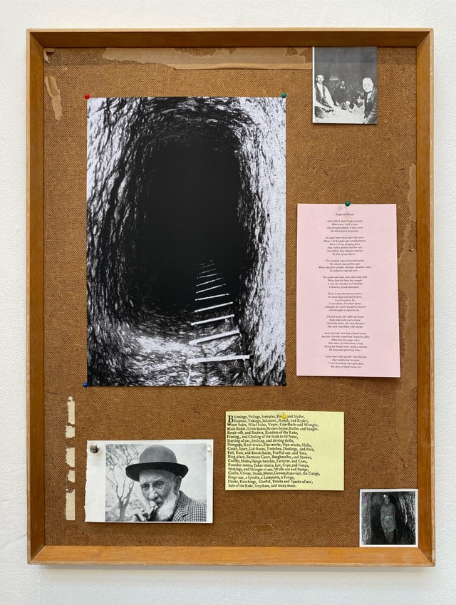 Assemblage by Jonny Davey using items fixed to a cork pinboard - photographs of a deep mine black tunnel and a man in a hat, alongside writing on coloured paper.