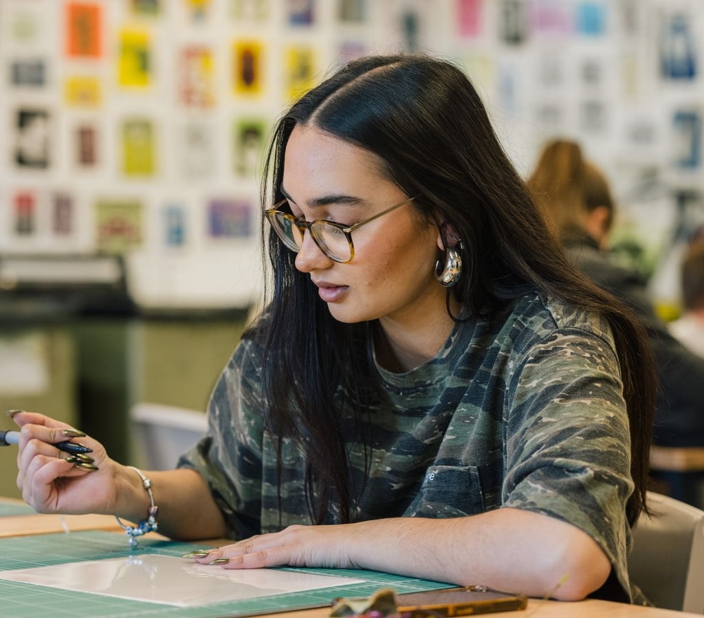 Female student with dark hair and glasses working on a creative project.
