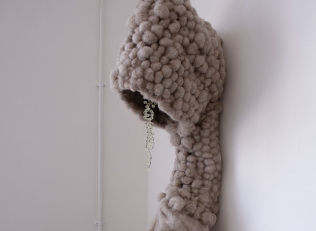 Sculpture leaning against a wall looking like a hooded figure.