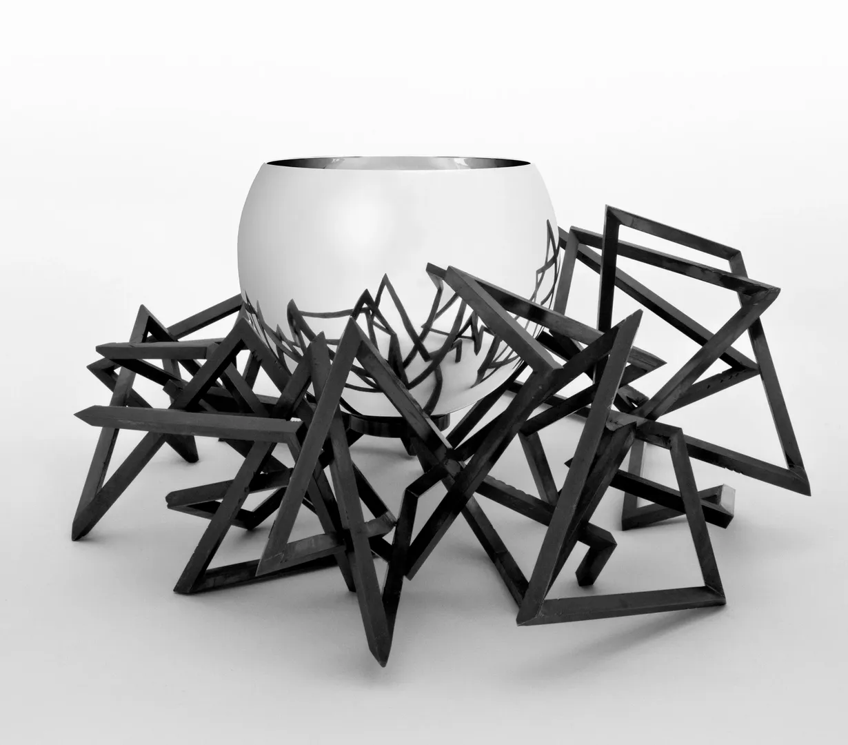 Silver bowl by Chris Knight, sat in a black geometric nest-like structure, which is reflected in the surface of the bowl.
