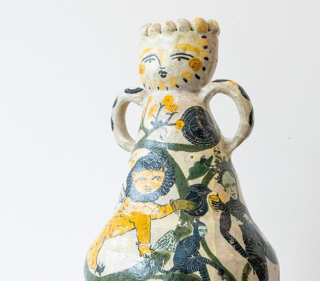 Ceramic vase by Evelyn Albrow, with large handles and a face at the top, handpainted with Medieval imagery of lions and pixies.
