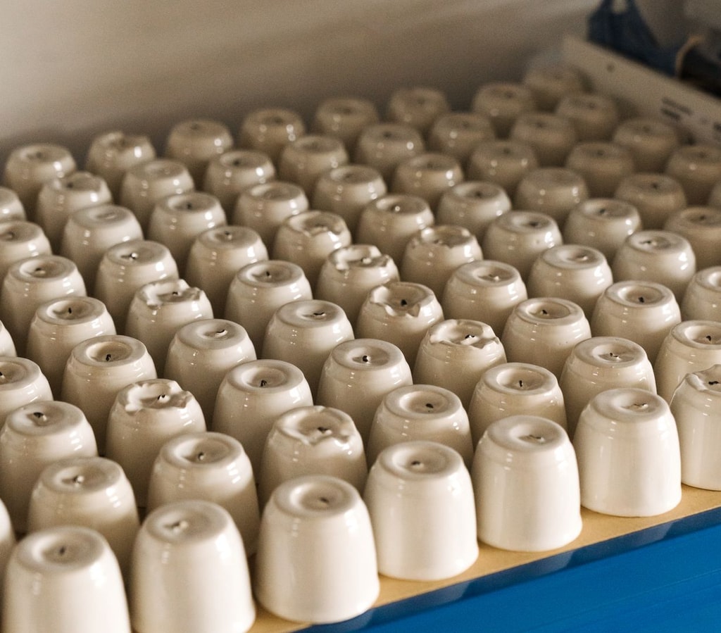 Many rows of small white candles made in ceramic, stored on a blue shelf.