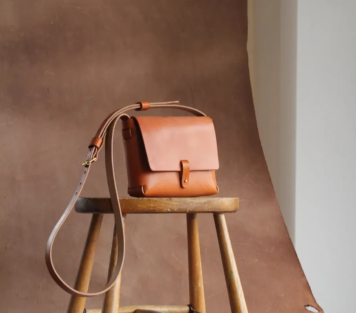 Handbag by Jonathan Hyde in tan leather, displayed on a wooden stool.