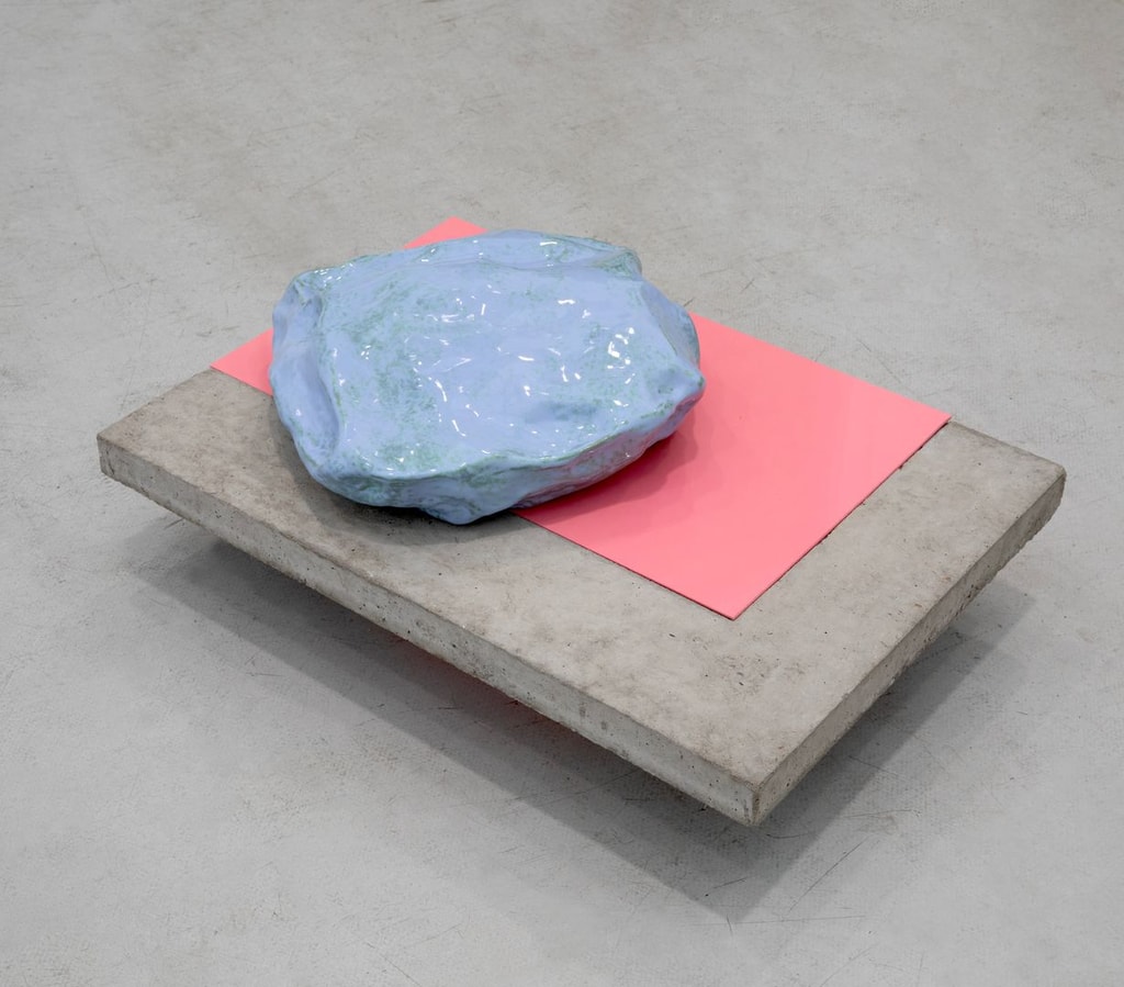 A concrete slab hovering above the ground. Atop it is a pink rectangle and a large blue boulder. By Maud Haya-Baviera