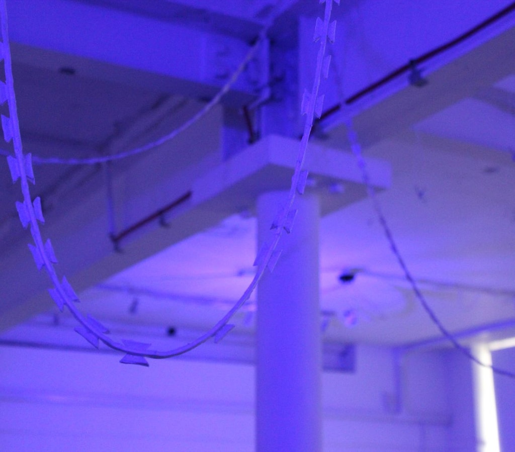 Blue lit ceiling girders with razor wire garlands dangling.