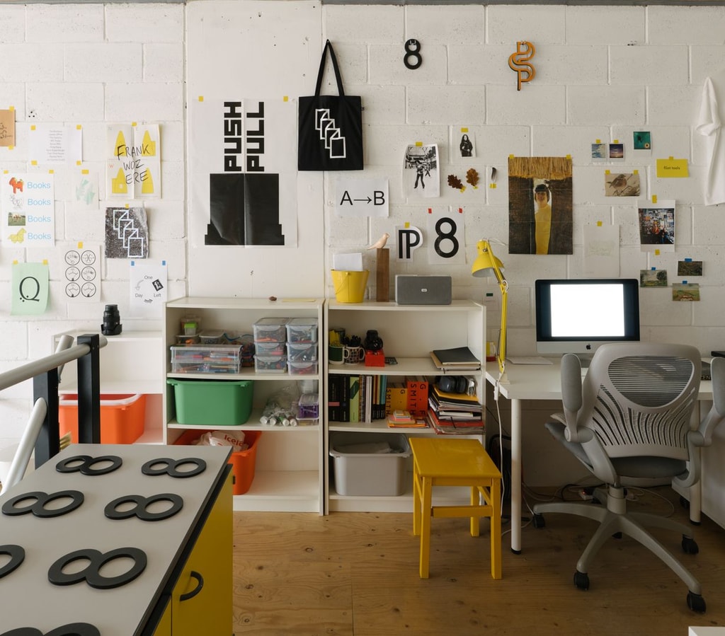 Bright studio with white breezeblock walls, showcasing a range of works on paper and a tshirt reading 'I'm Sorry Simon'. Desk with computer.