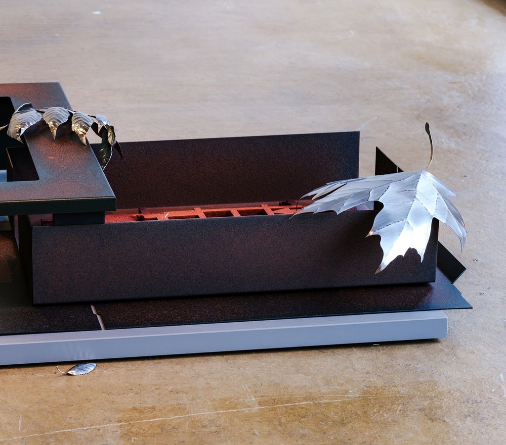 A metal floor sculpture evoking an office desk scattered with fallen leaves.