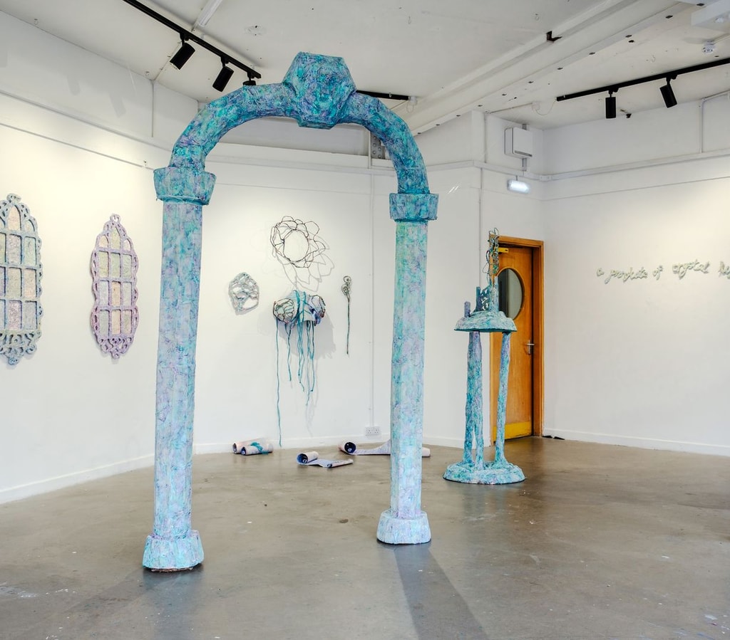 Installation view of a sculptural archway and various paper mache items on the walls.
