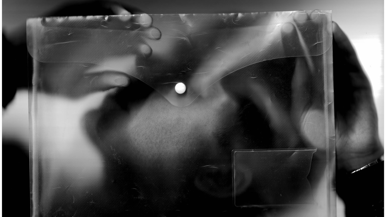 A photograph taken with a scanner, featuring a plastic wallet and a man's face laying on the glass.